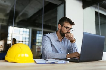 Man working at laptop with hard hat on desk